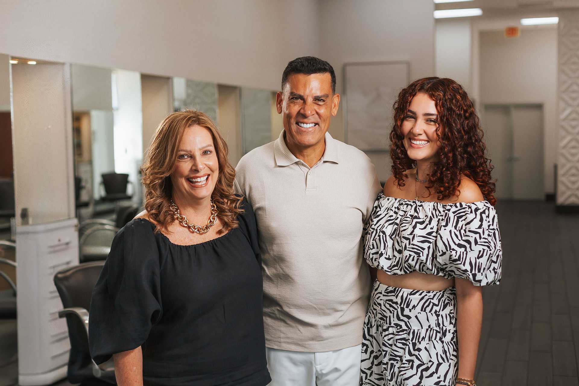 Three people smiling while standing together in a well-lit salon with modern décor.